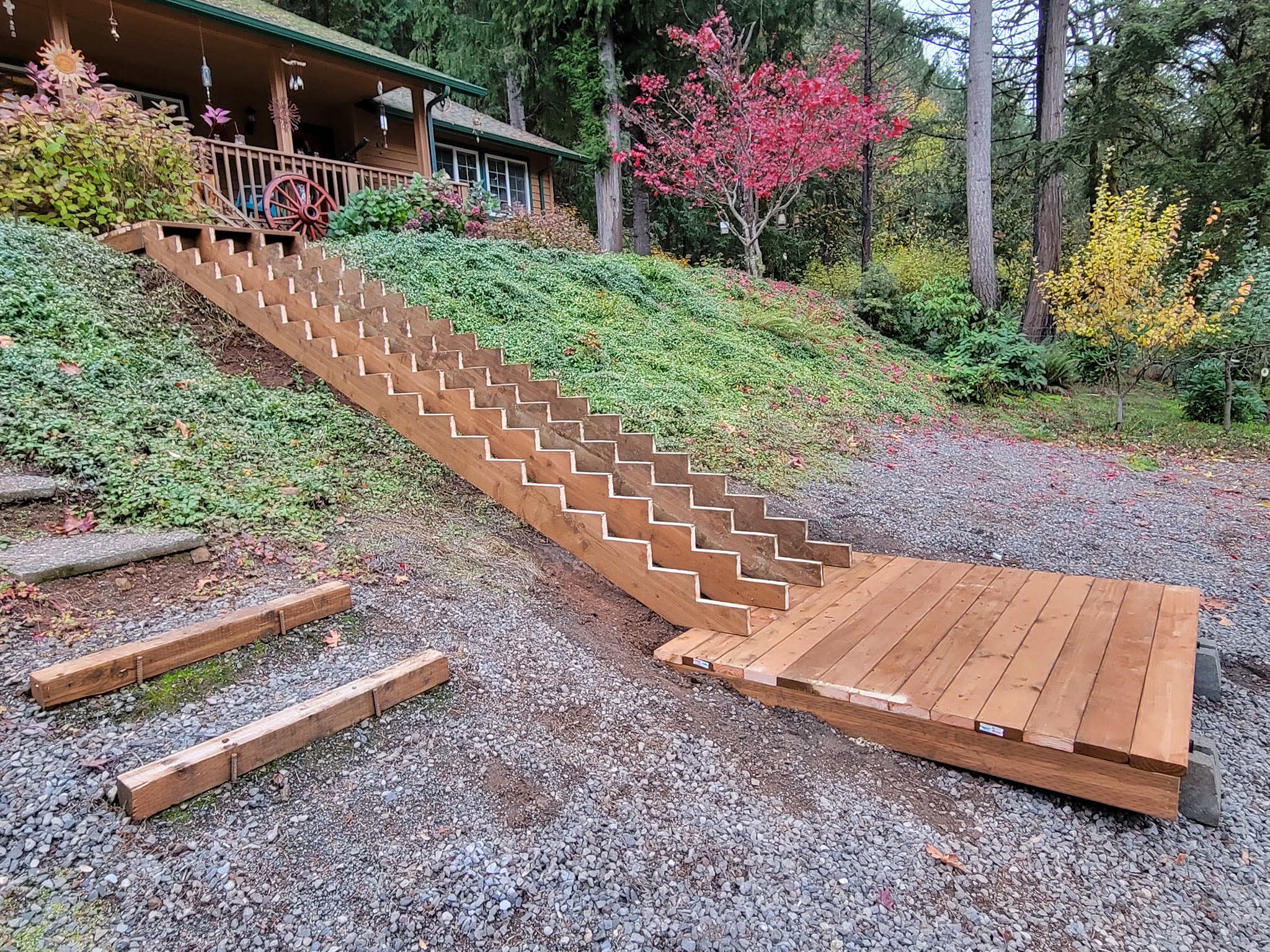 Long finished wooden staircase down a landscaped hillside to a gravel pad near a cabin