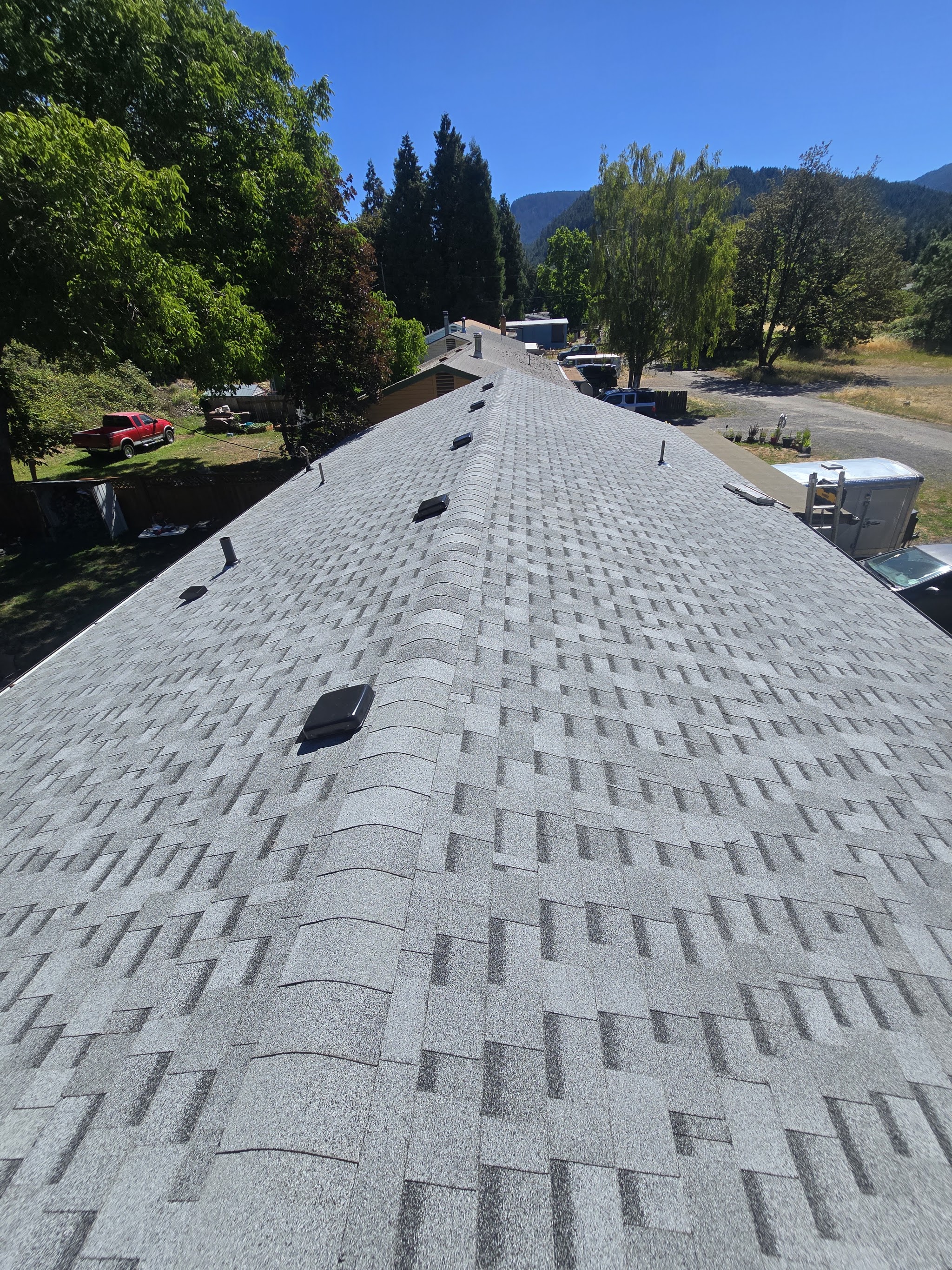 New gray architectural shingle roof on a long ridge line, forested mountain valley behind it